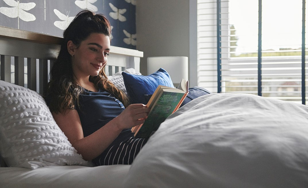 Woman reading a book in bed with a cosy bedroom setting