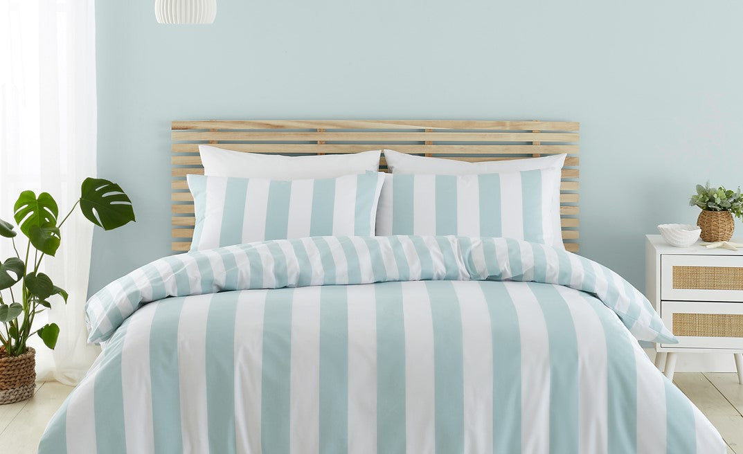 Blue and white striped bedding set on a bed with a light blue wall and white nightstand.