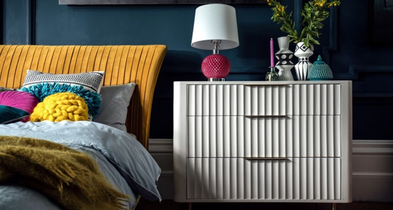 Modern bedroom with a yellow bed, white chest of drawers, and colourful decor.