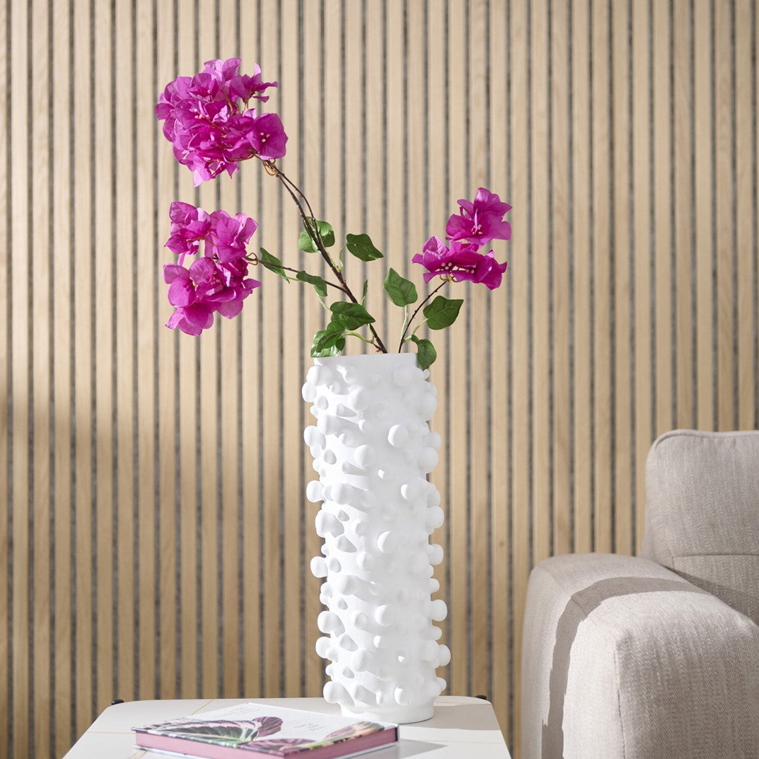White textured vase with pink fake flowers on a table against a wooden panelled wall.