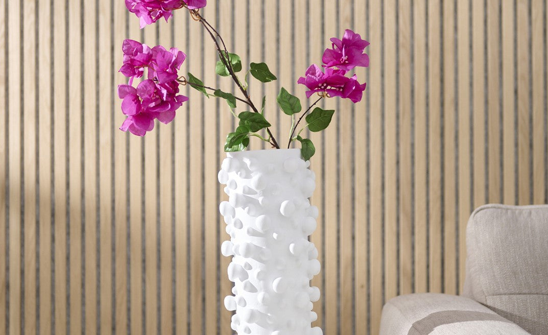 White textured vase with pink flowers against a beige wall.