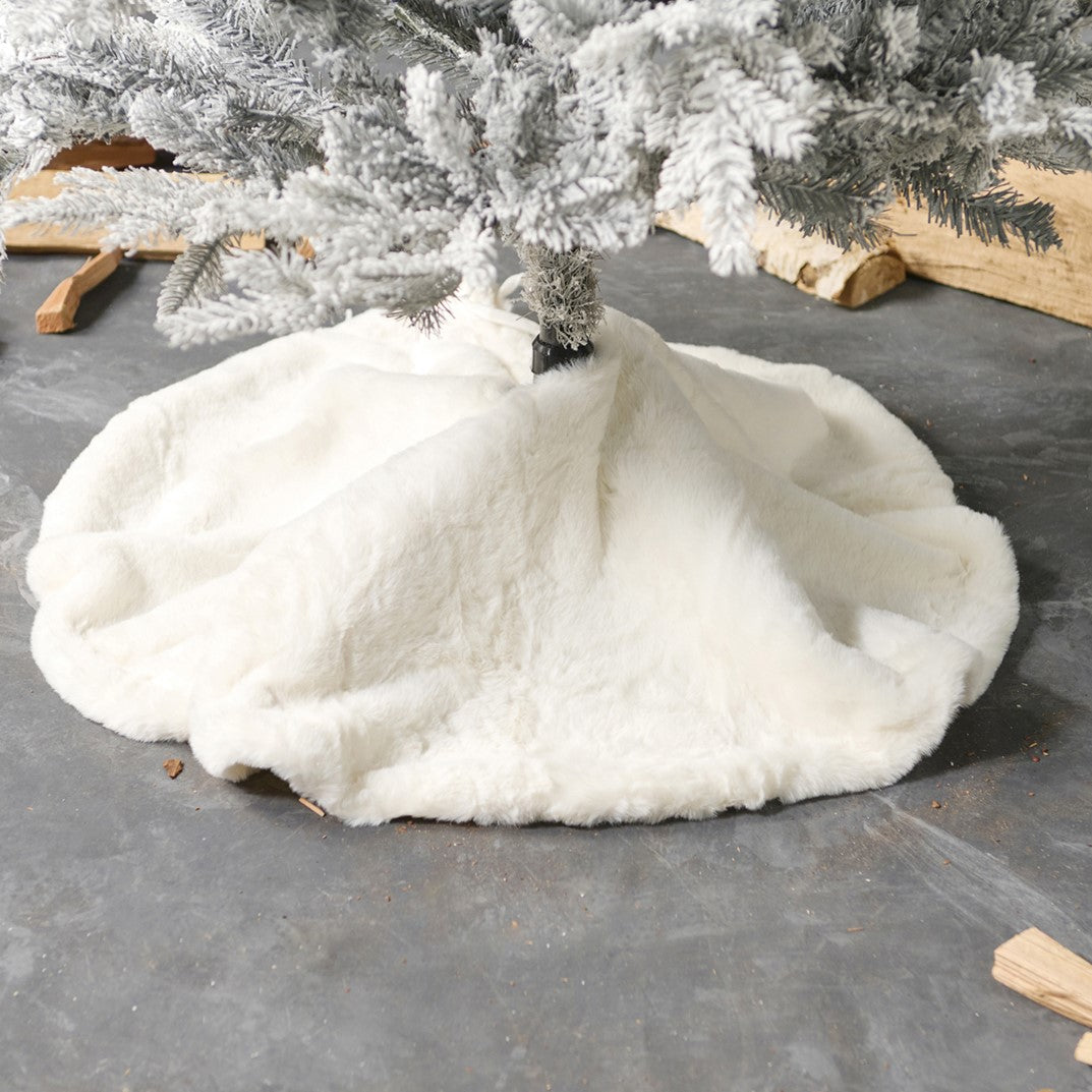 White tree skirt on a gray surface with a Christmas tree in the background