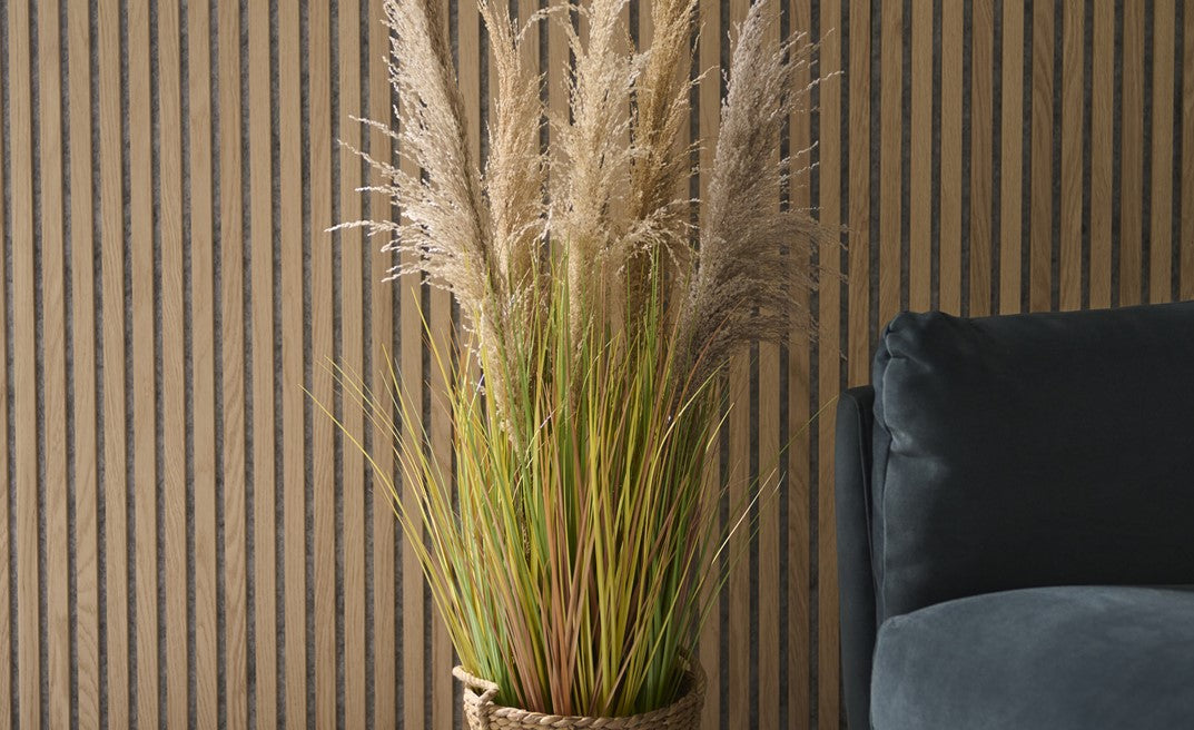 Potted plant with dried grasses against a striped wall with a dark blue sofa.
