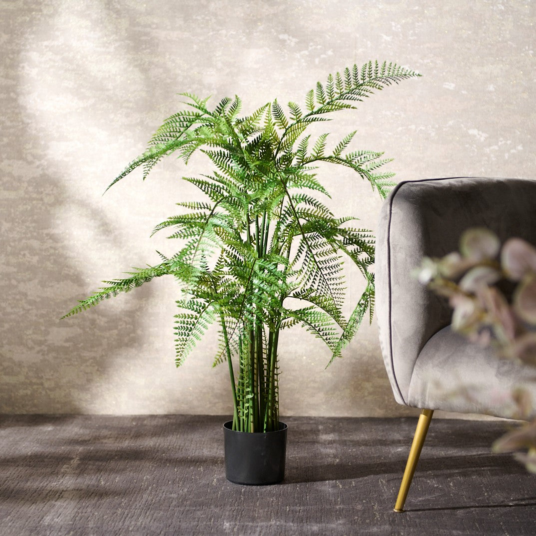 Potted fake fern plant in a room with a grey chair and decorative elements.