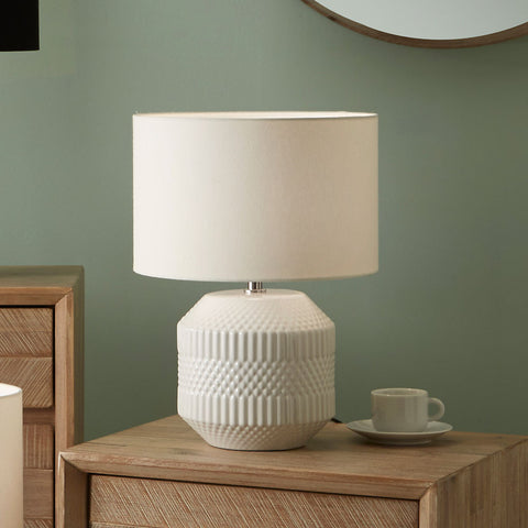 White textured table lamp on a wooden side table with a green wall background