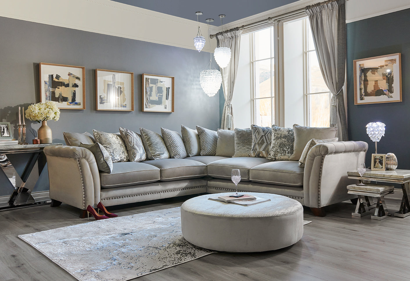 Living room with a corner grey velvet sofa, ottoman, and decorative elements.