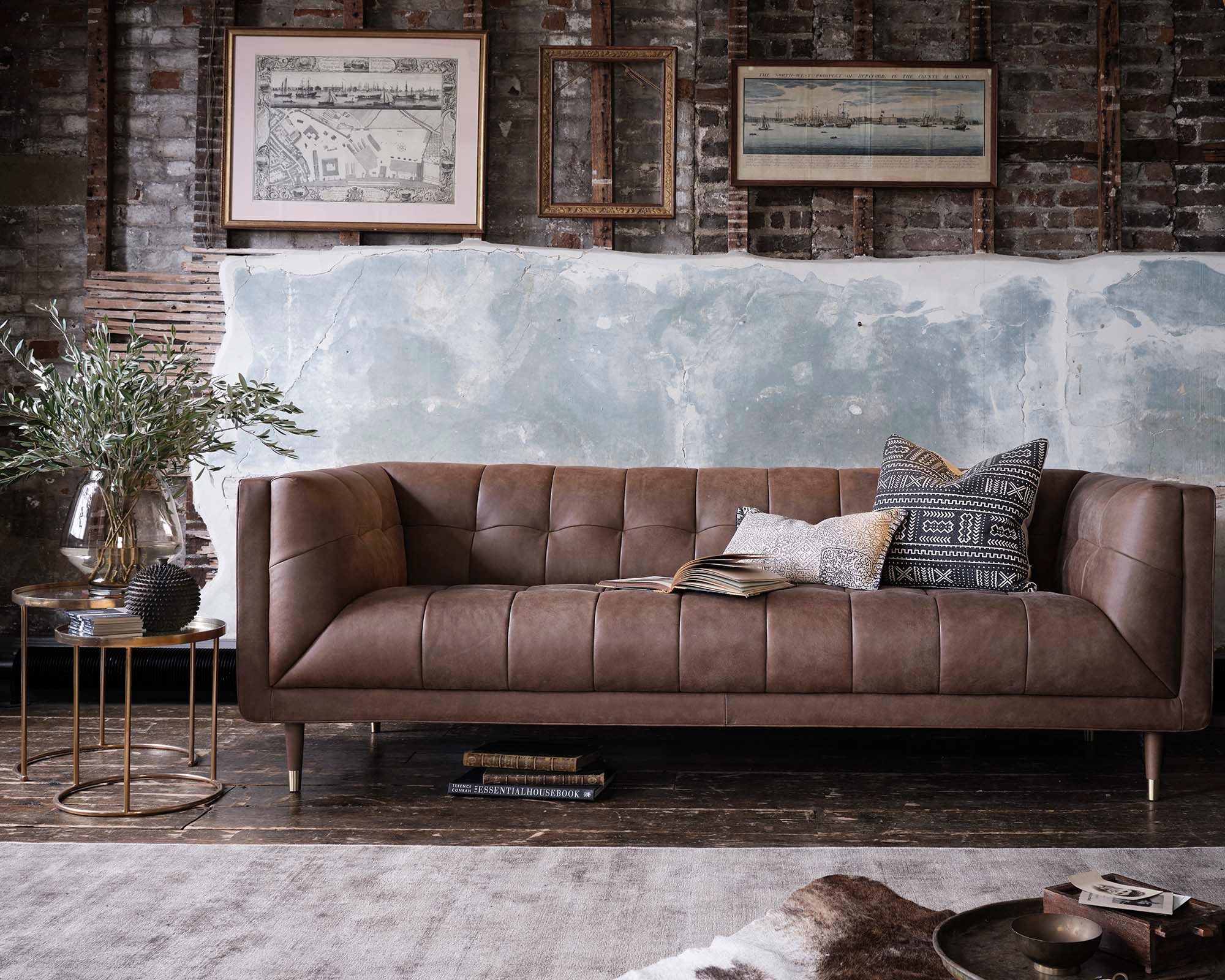 Brown leather sofa in a room with brick walls and framed artwork.