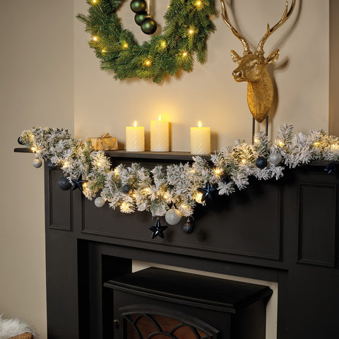 Decorative Christmas mantel with garland, candles, and wreath on a fireplace.