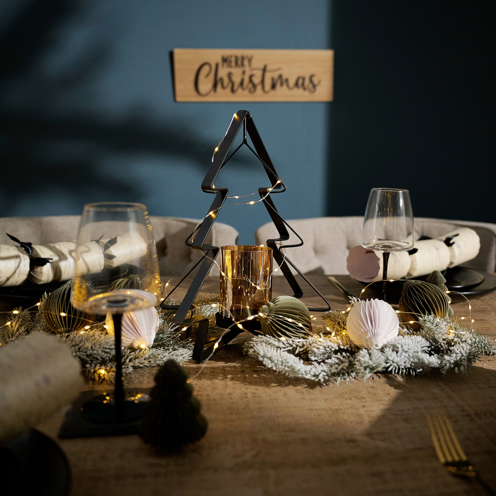 Decorative Christmas table setting with a tree-shaped candle holder, glasses, and festive decorations.