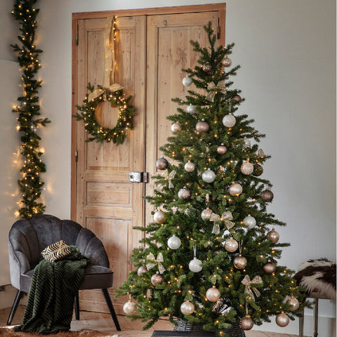 Decorated Christmas tree with lights and ornaments in a room with a wooden door and chair.