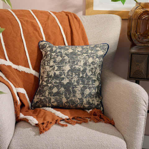 Decorative pillow on a chair with an orange throw blanket