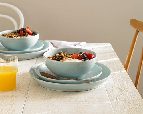 Denby light blue ceramic bowls with breakfast cereal and fruit on a wooden table.