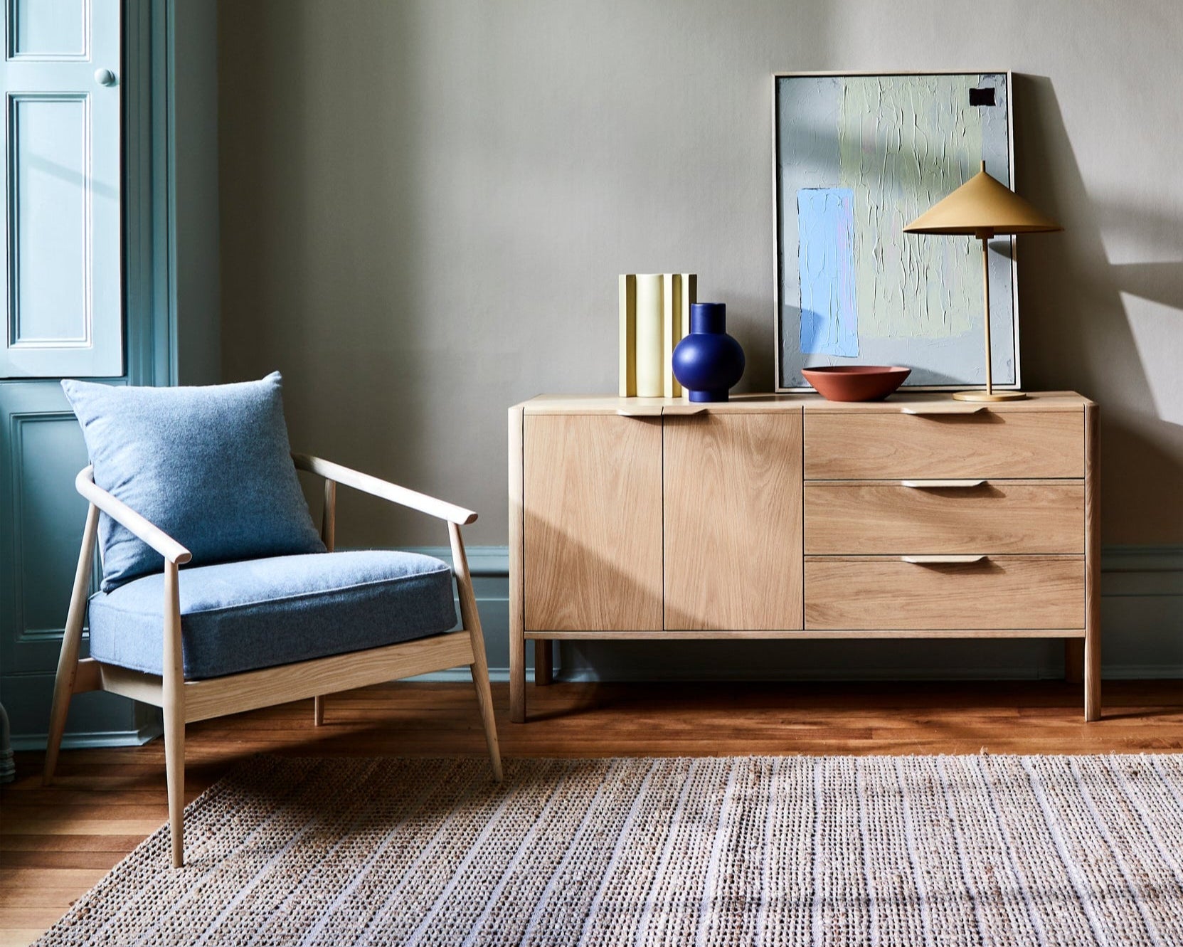 Mia wooden sideboard with decorative items in a room with a chair and rug.