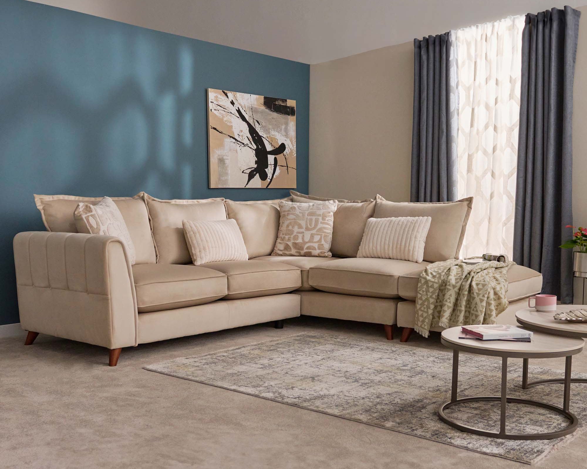 Gabrielle beige corner sofa in a living room with a blue wall, painting, and coffee table.