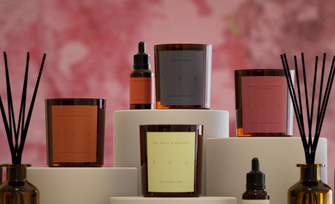 Collection of decorative items including candles, diffusers, and bottles on a pink floral background