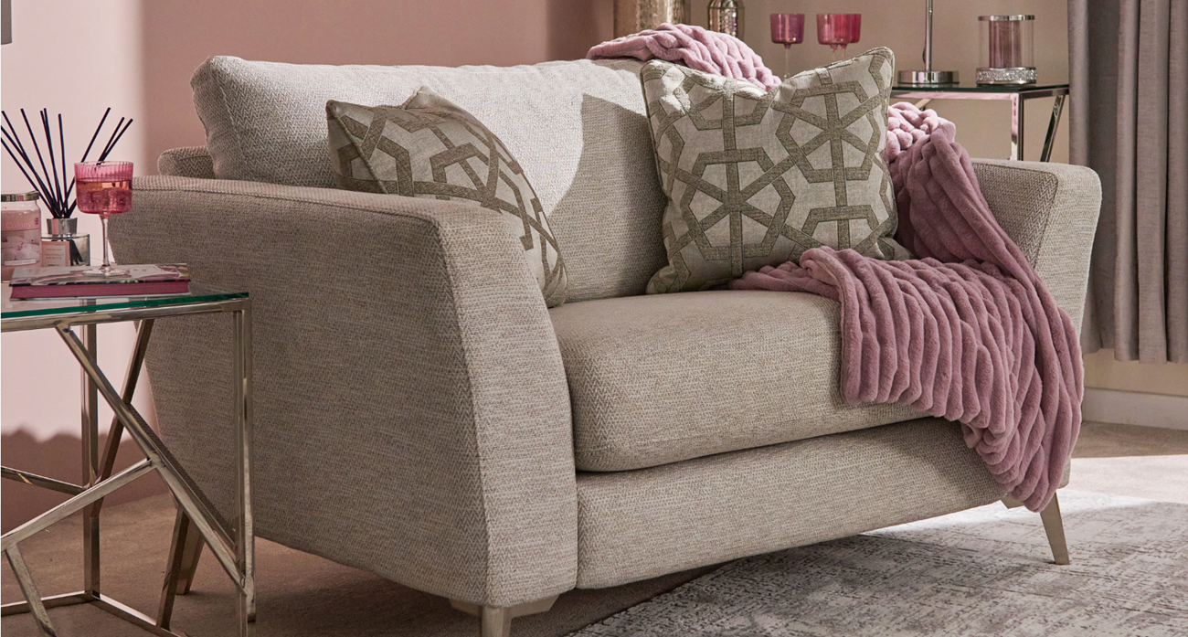 Beige sofa with patterned cushions and a pink blanket in a living room setting.