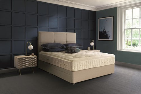 Beige Hypnos bed with pillows in a room with dark blue panelled walls and a window.