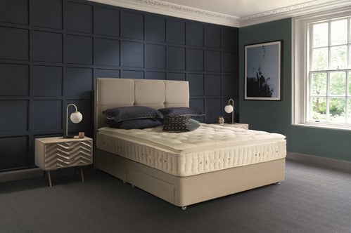 Beige Hypnos bed with pillows in a room with dark blue panelled walls and a window.
