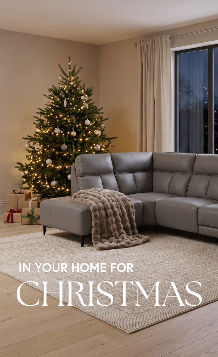 A gray sectional sofa in a living room beside a decorated Christmas tree, with a beige throw blanket draped over the seat and large white text reading 'IN YOUR HOME FOR CHRISTMAS' at the bottom.