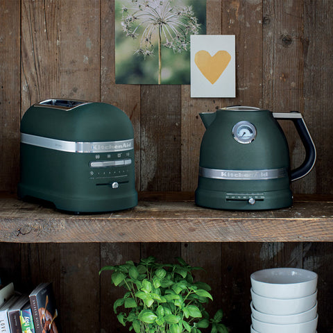 KitchenAid green toaster and kettle on a wooden shelf with decorative elements in the background.