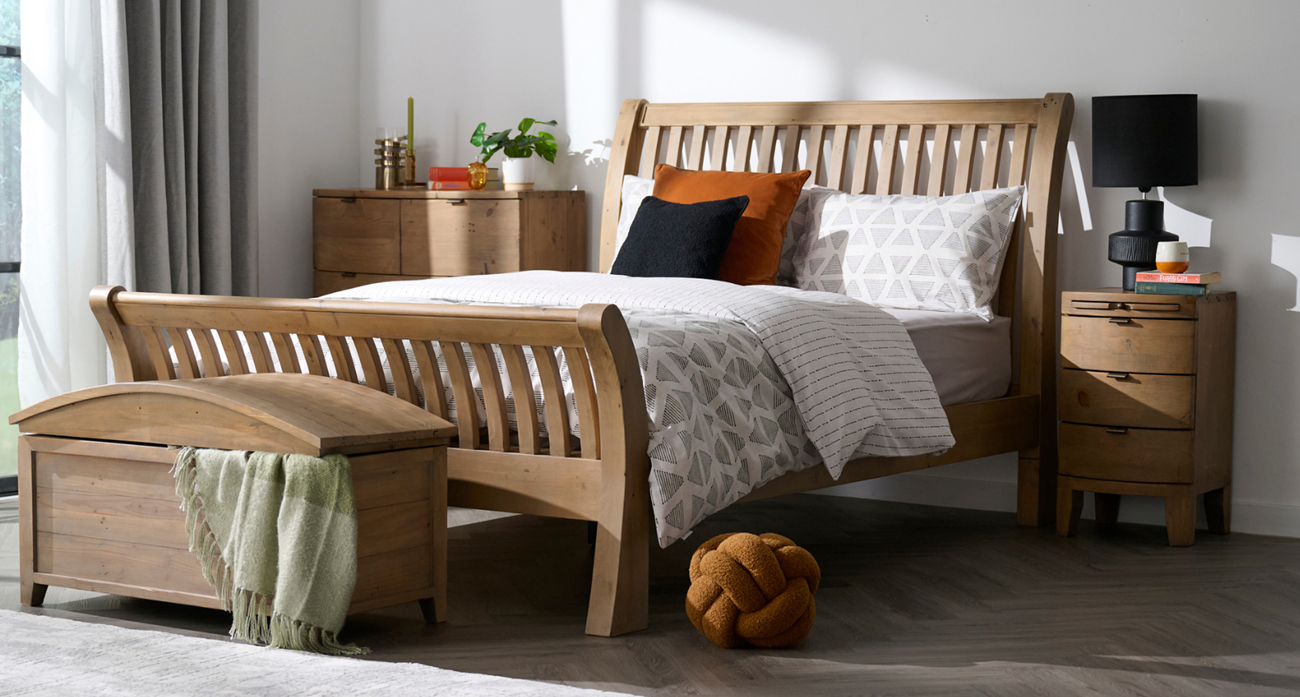 Wooden bed with matching bedside table and chest of drawers in a bright room setting