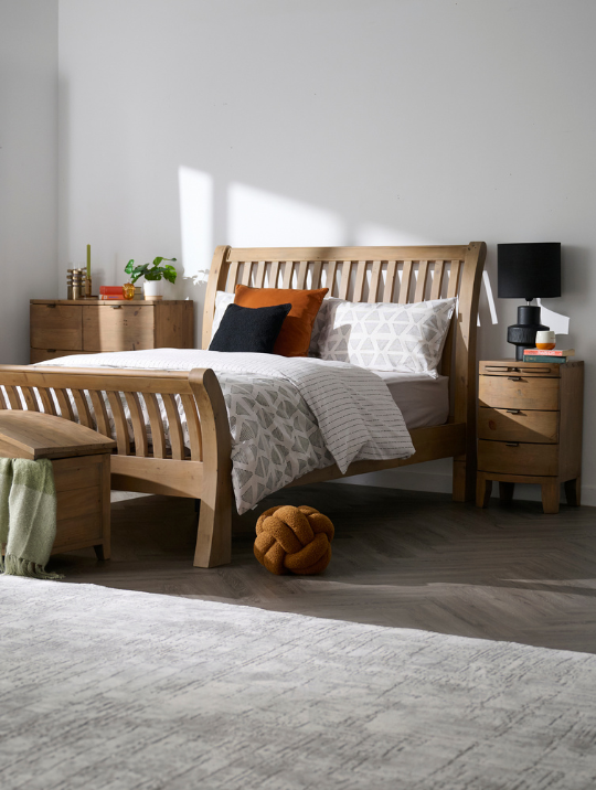 Wooden bed with matching bedside table and chest of drawers in a bright room setting