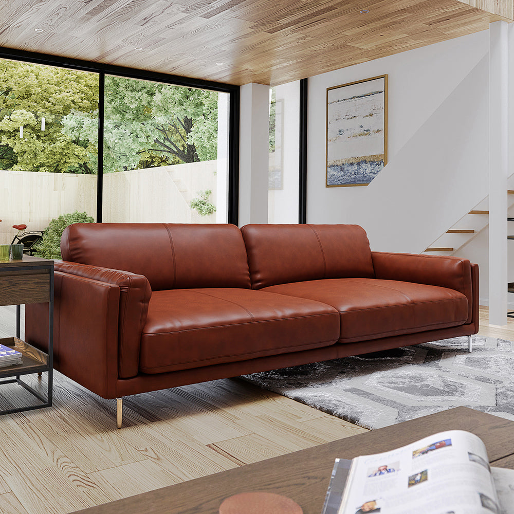 Brown leather sofa in a modern living room with large windows and a rug.