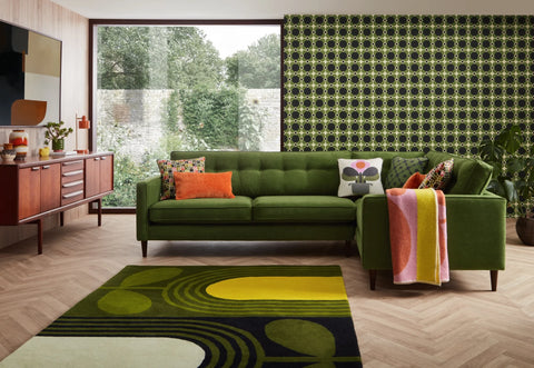 Green sofa with colorful cushions in a room with patterned wallpaper and rug.