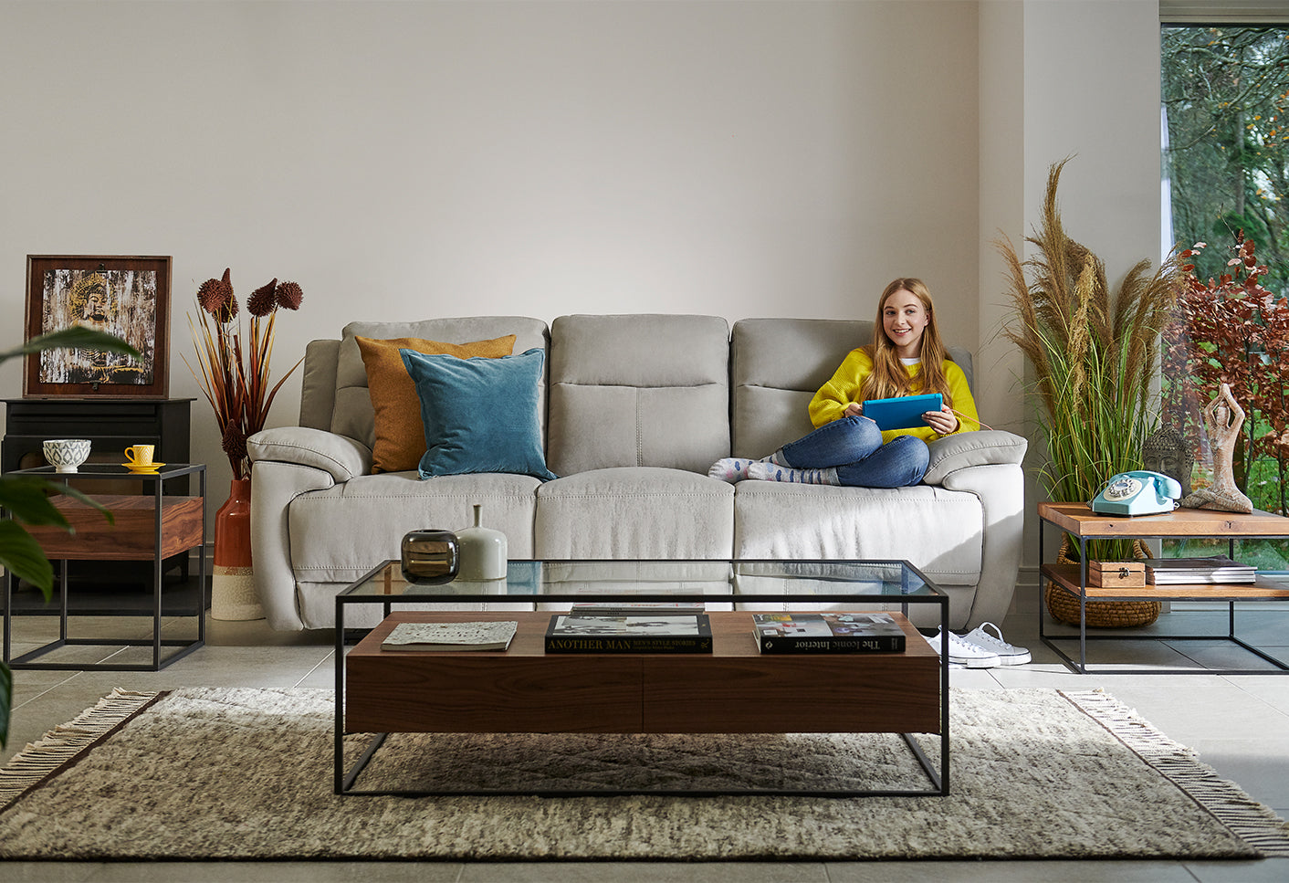 Woman sitting on a grey sofa in a modern living room with a glass coffee table and decorative items.