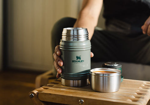 Person holding a Stanley food jar on a wooden table