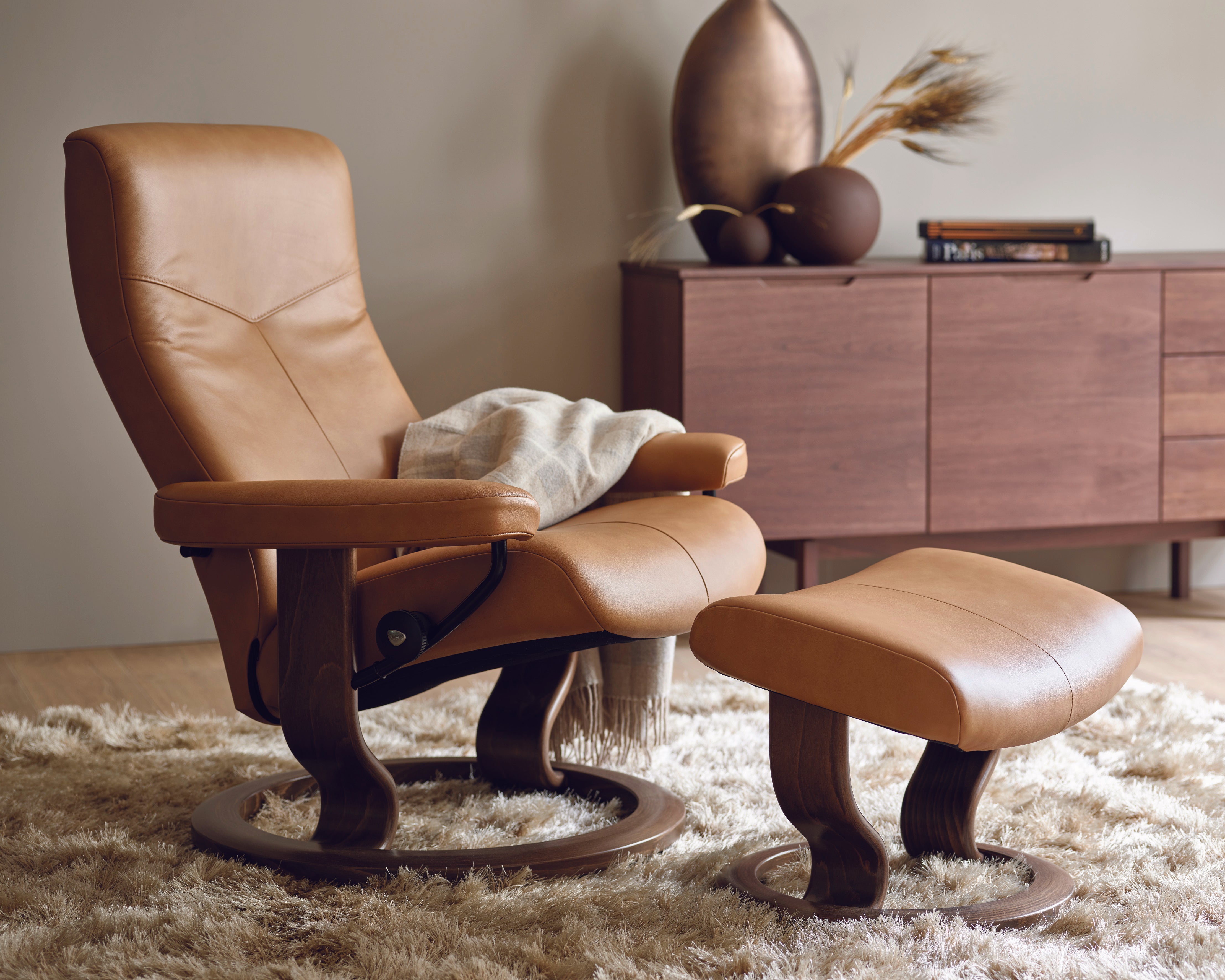 Stressless brown leather recliner chair with ottoman in a room with wooden furniture and decor.