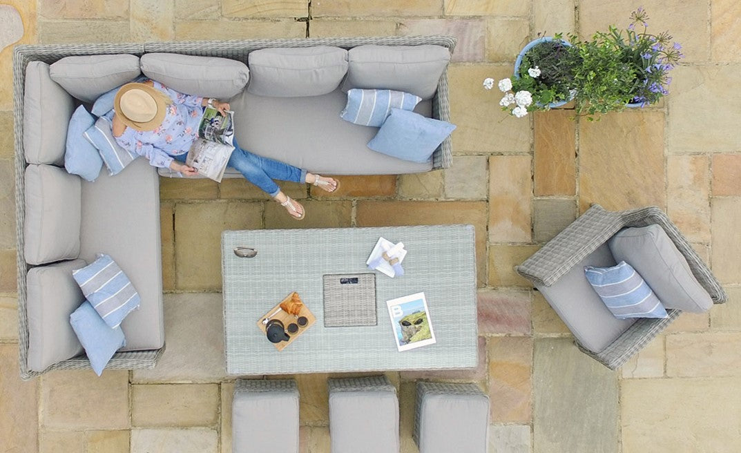 Outdoor grey rattan furniture set with cushions, a woman sitting on a sofa and a rattan table.