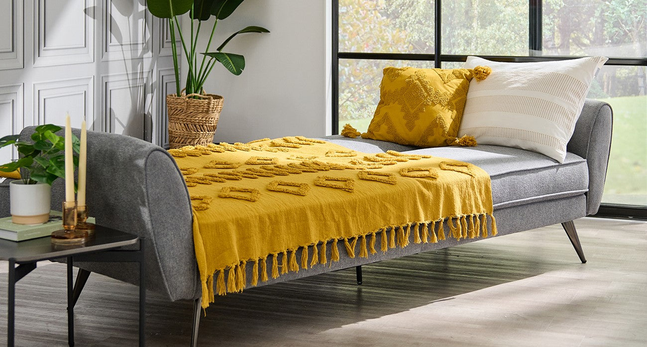Grey sofa bed with yellow blanket and cushions in a bright room.
