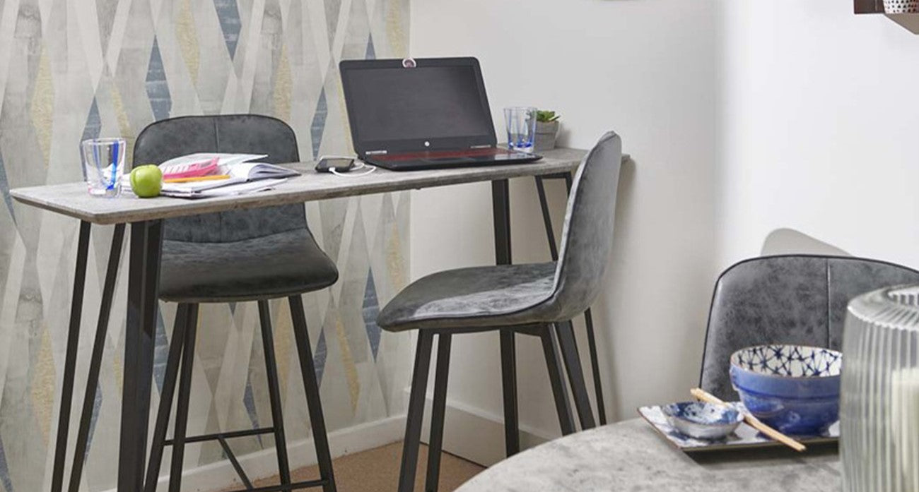 Small home office with a desk, chairs, and a laptop against a geometric-patterned wall.