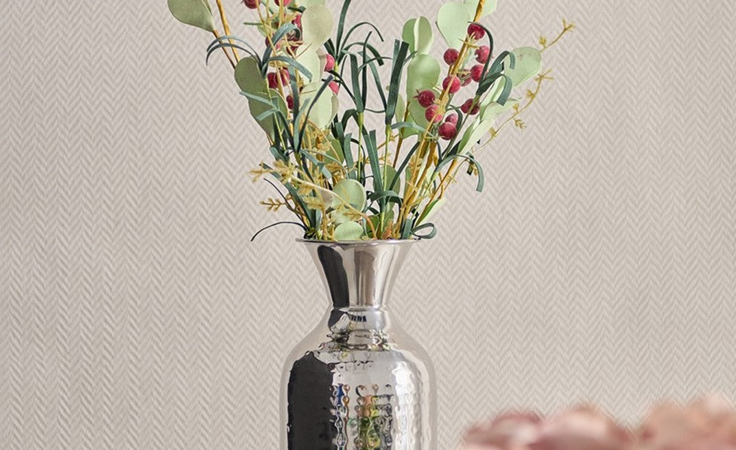 Silver vase with decorative plants on a textured beige background
