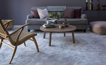 Grey fabric sofa with wooden coffee table and wooden chair in a living room with a sofa grey carpet.