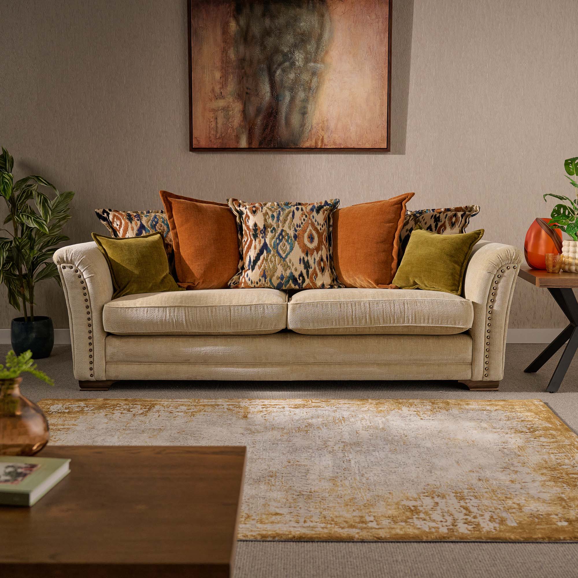 Living room with a beige sofa adorned with colorful pillows, a textured rug, and a painting on the wall.