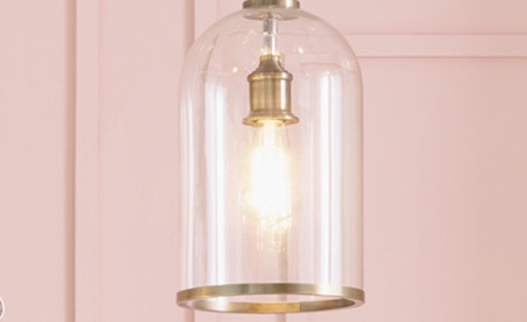 Clear glass pendant light with gold trim against a pink wall