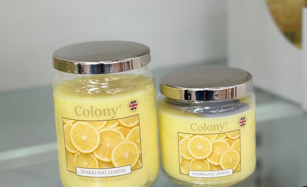 Two Colony sparkling yellow lemon candles on a reflective surface with a neutral background