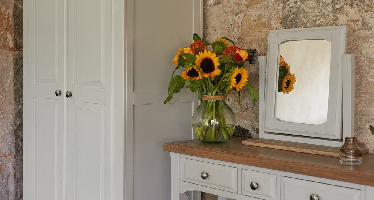 sunflowers in a vase on top of a wooden dressing table