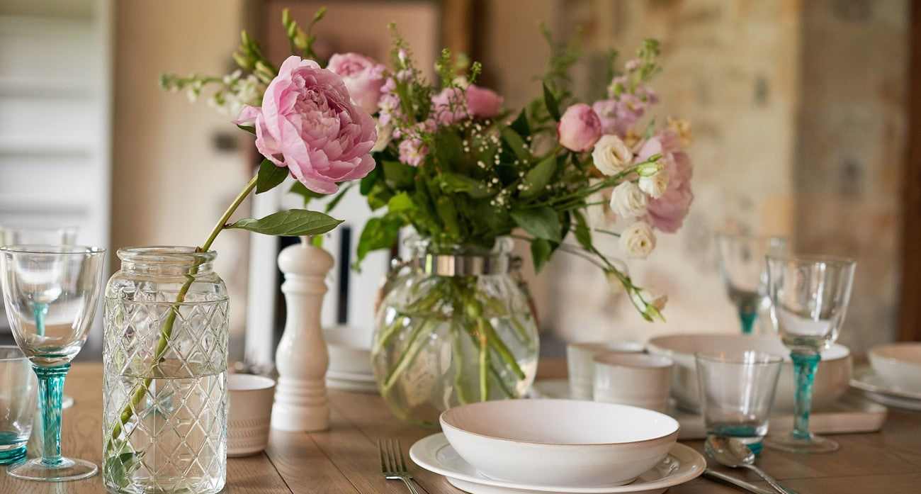 Decorative table setting with flowers, glasses, and plates in a warm-toned room.