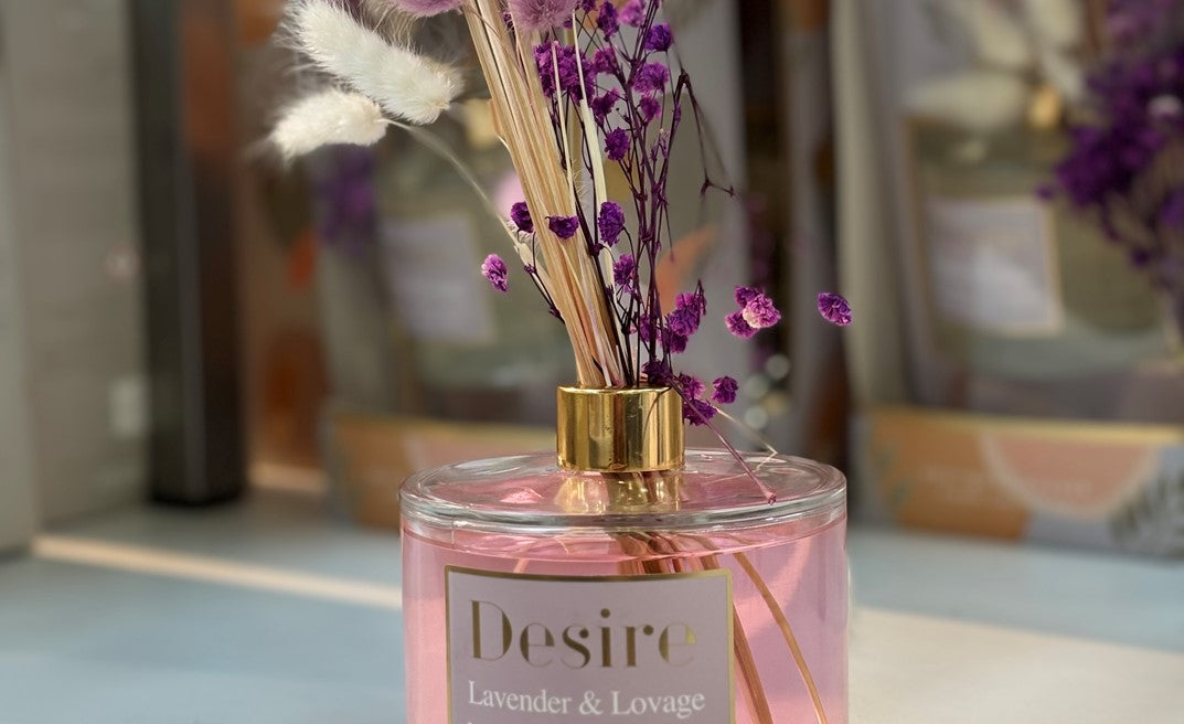 Decorative pink diffuser with dried flowers and 'Desire' branding in a blurred indoor setting