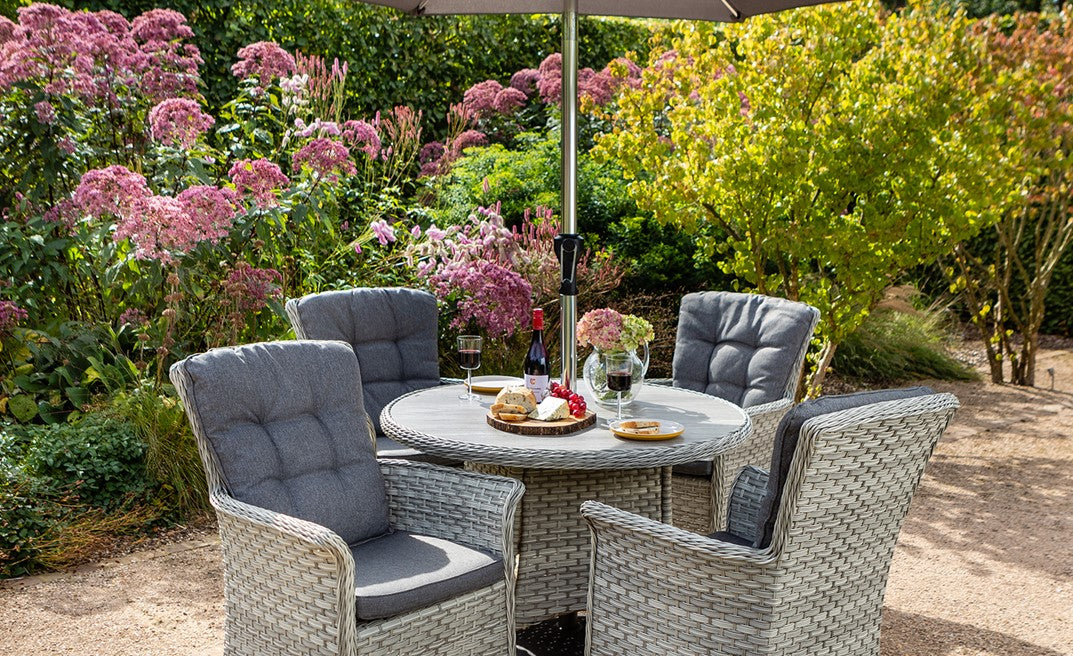 Outdoor rattan furniture set with table and chairs in a garden setting.