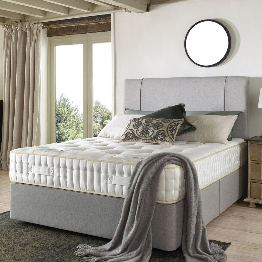 Grey fabric bed frame and head board with a white mattress, with a grey throw blanket draped over the foot of the bed.