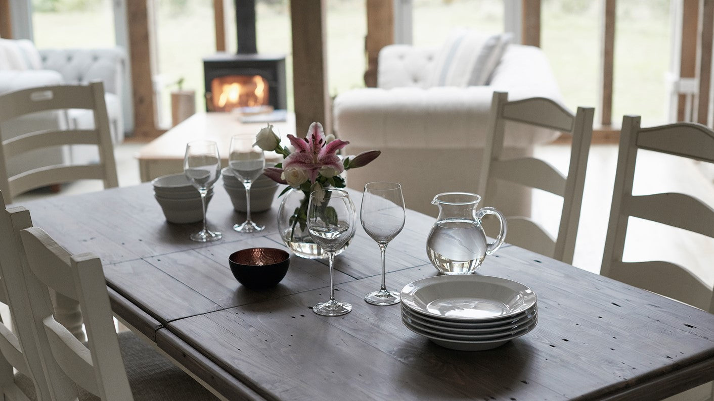 Dining table set with plates, glasses, and a vase of flowers on a dining table with white chairs.