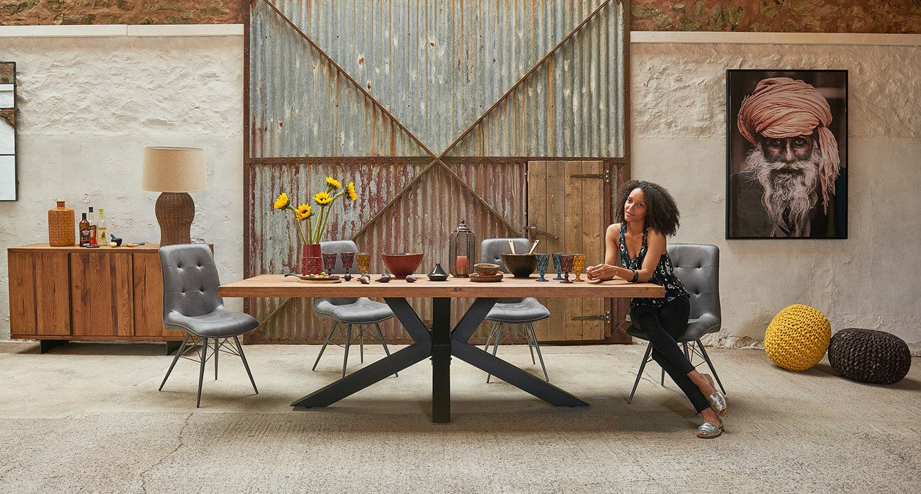 Woman sitting at a wooden dining table with grey leather chairs with rustic decor.