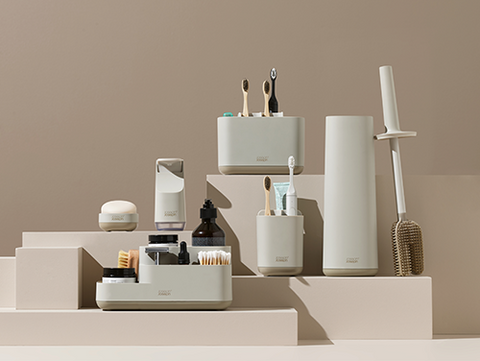 Collection of Joseph Joseph bathroom products including toothbrushes, bottles, and containers on a beige background