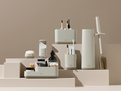 Collection of Joseph Joseph bathroom products including toothbrushes, bottles, and containers on a beige background