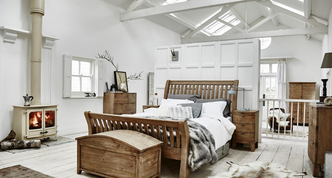 Wooden bed in a bright bedroom with white walls and wooden furniture.