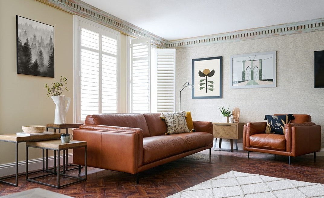 Modern living room with brown leather sofa and armchair, wooden coffee table, and decorative elements.